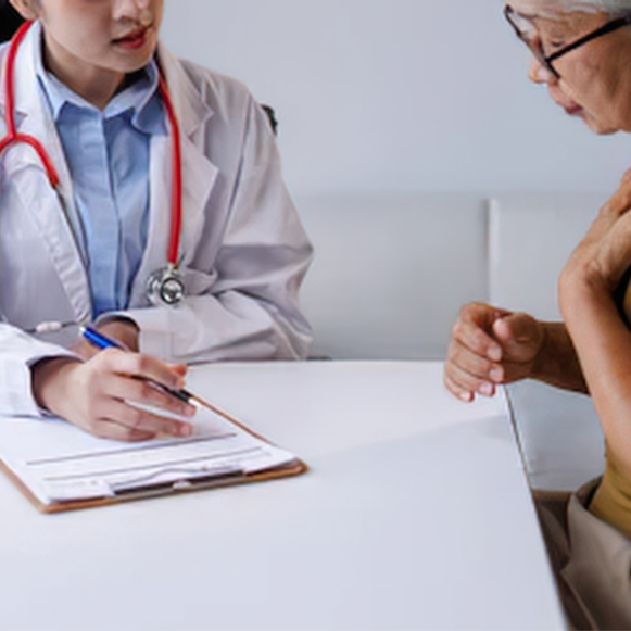 Doctor in a white coat reviewing a form on a clipboard with a patient seated across the table