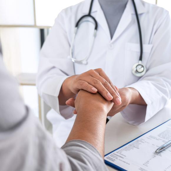 Infertility Doctor in a white coat holding a patient's hand across a desk, with a clipboard nearby