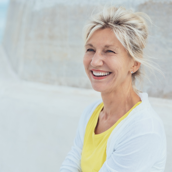 Menopause Smiling woman in a yellow top and white cardigan standing outdoors near a stone wall