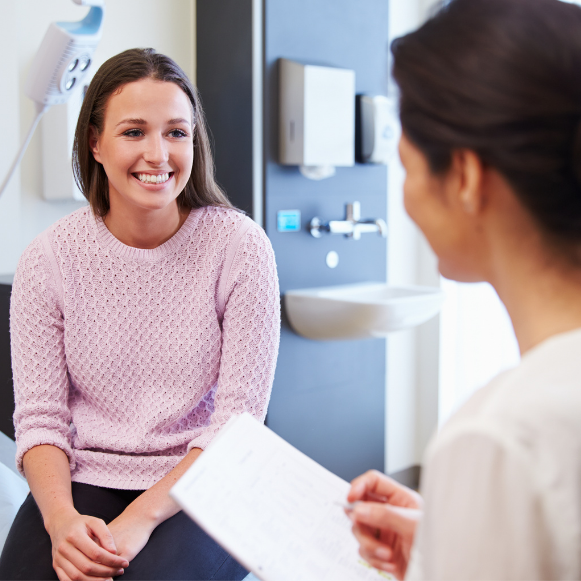 PMS Smiling patient seated in an exam room talking with a provider holding a chart