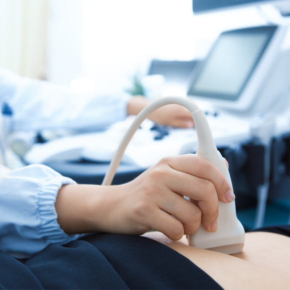 Sonographer holding an ultrasound probe against a patient's abdomen beside an ultrasound machine